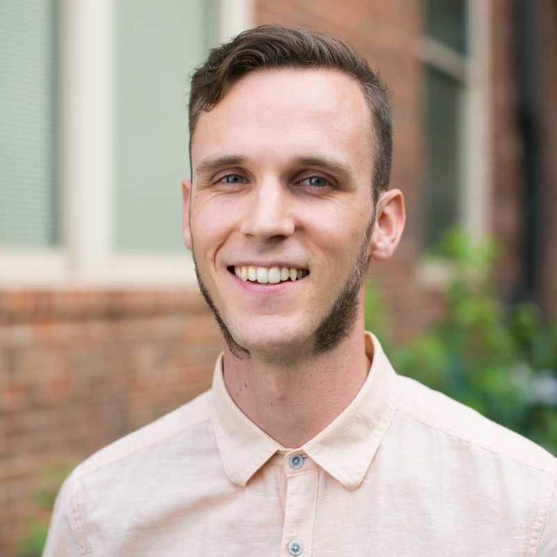 A photo of Corey Light, a smiling person wearing a light-peach button-up shirt