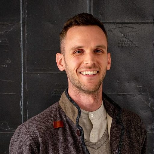 A photo of Corey Light, a smiling person wearing a light-peach button-up shirt